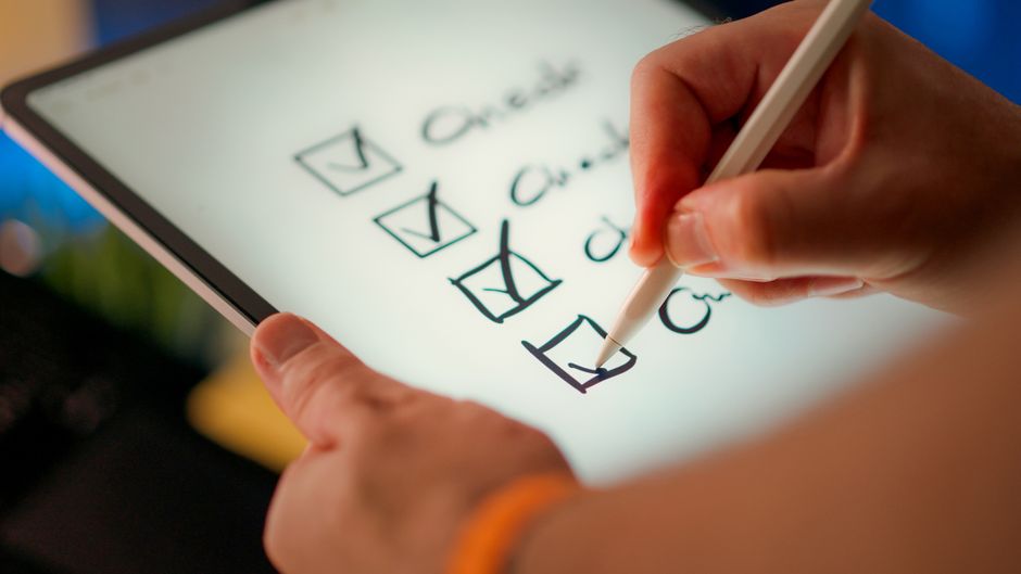 Close-up of a digital checklist being marked off on a tablet with a stylus pen.